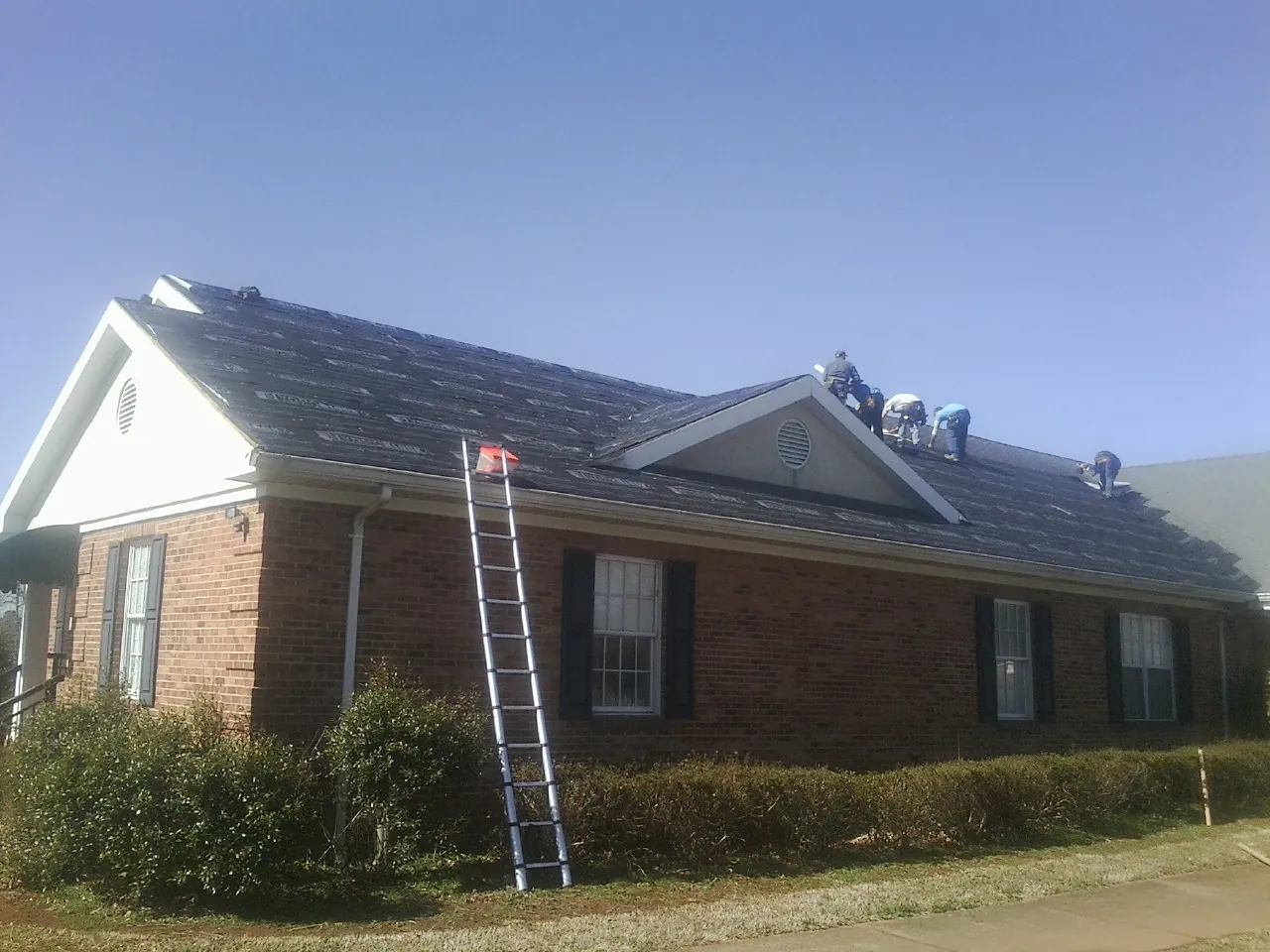 Crew tearing shingles off a brick ranch roof with a ladder set — Emergency Roof Repair work by our crew in Medway